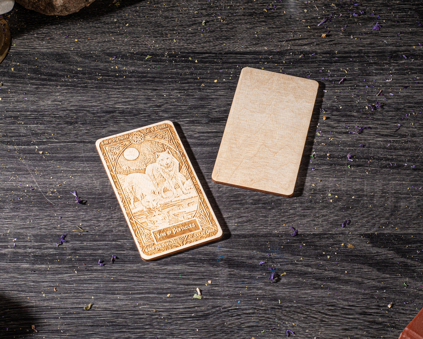 a wooden card with an embossed design, placed on a wooden surface with scattered purple flowers.