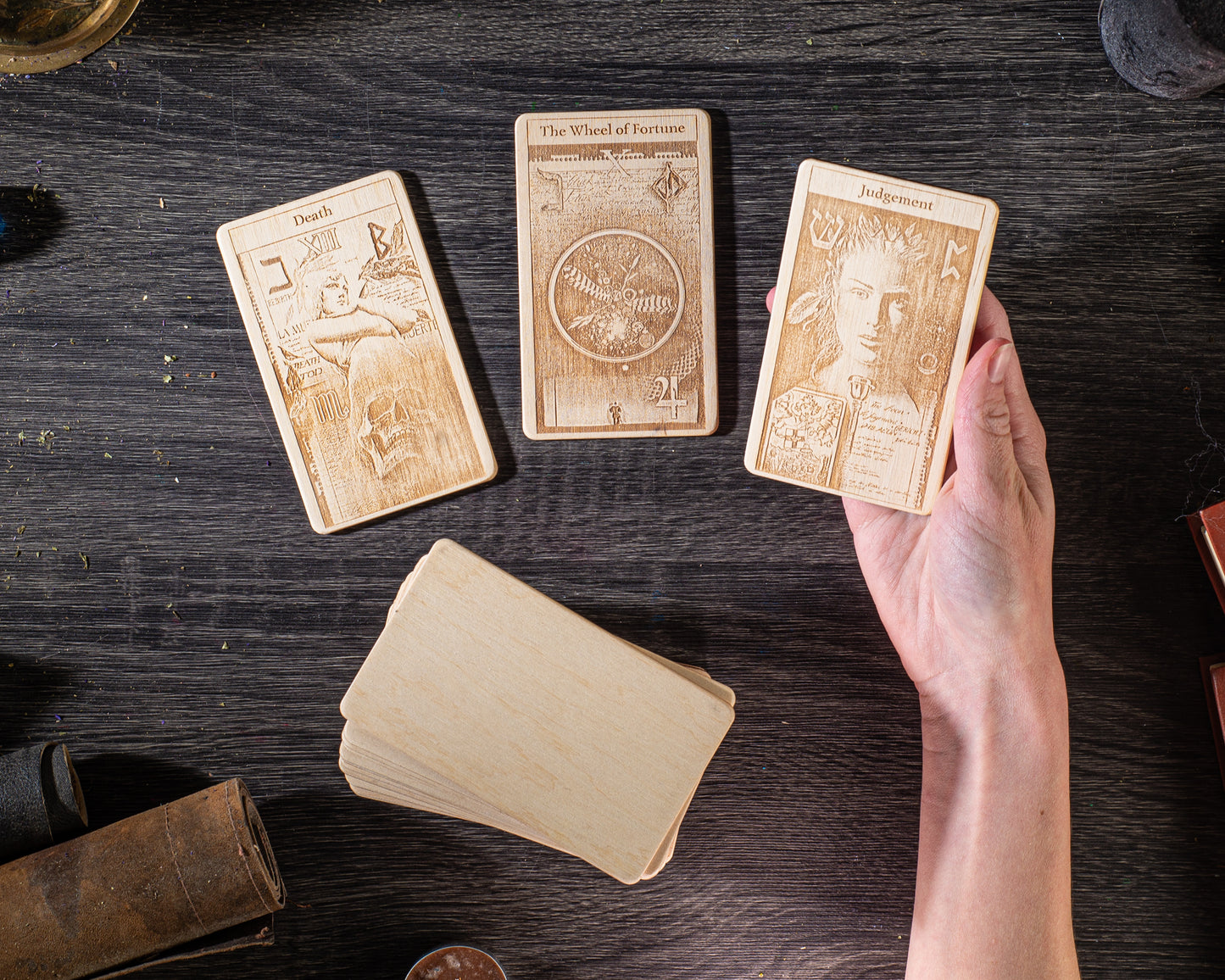 a person's hand holding three wooden tarot cards on a dark wooden surface.