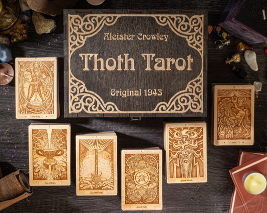 a collection of seven tarot cards arranged on a dark wooden surface, with a wooden box labeled "Thoth Tarot" in the background.
