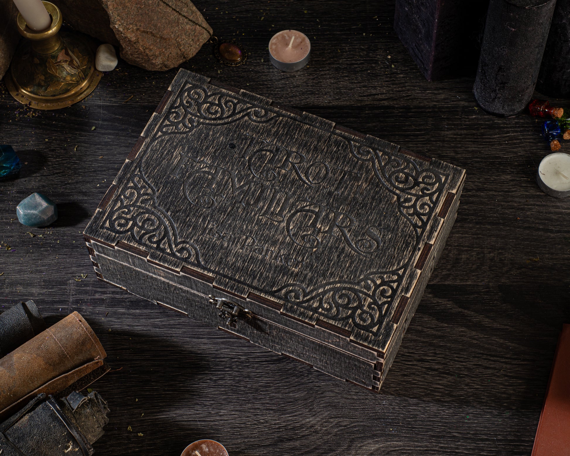a dark wooden box with an ornate design, placed on a wooden surface surrounded by various objects such as candles, gemstones, and other knick-knacks.