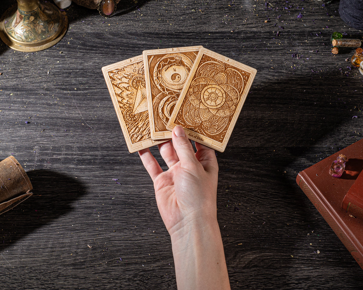 A hand holding three wooden tarot cards against a dark wooden background.