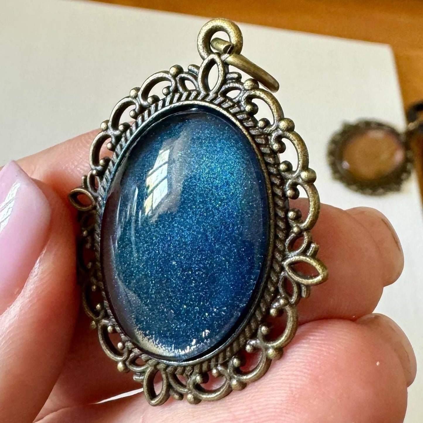 A hand is holding a decorative pendant with a blue gemstone, which appears to be a piece of jewelry.