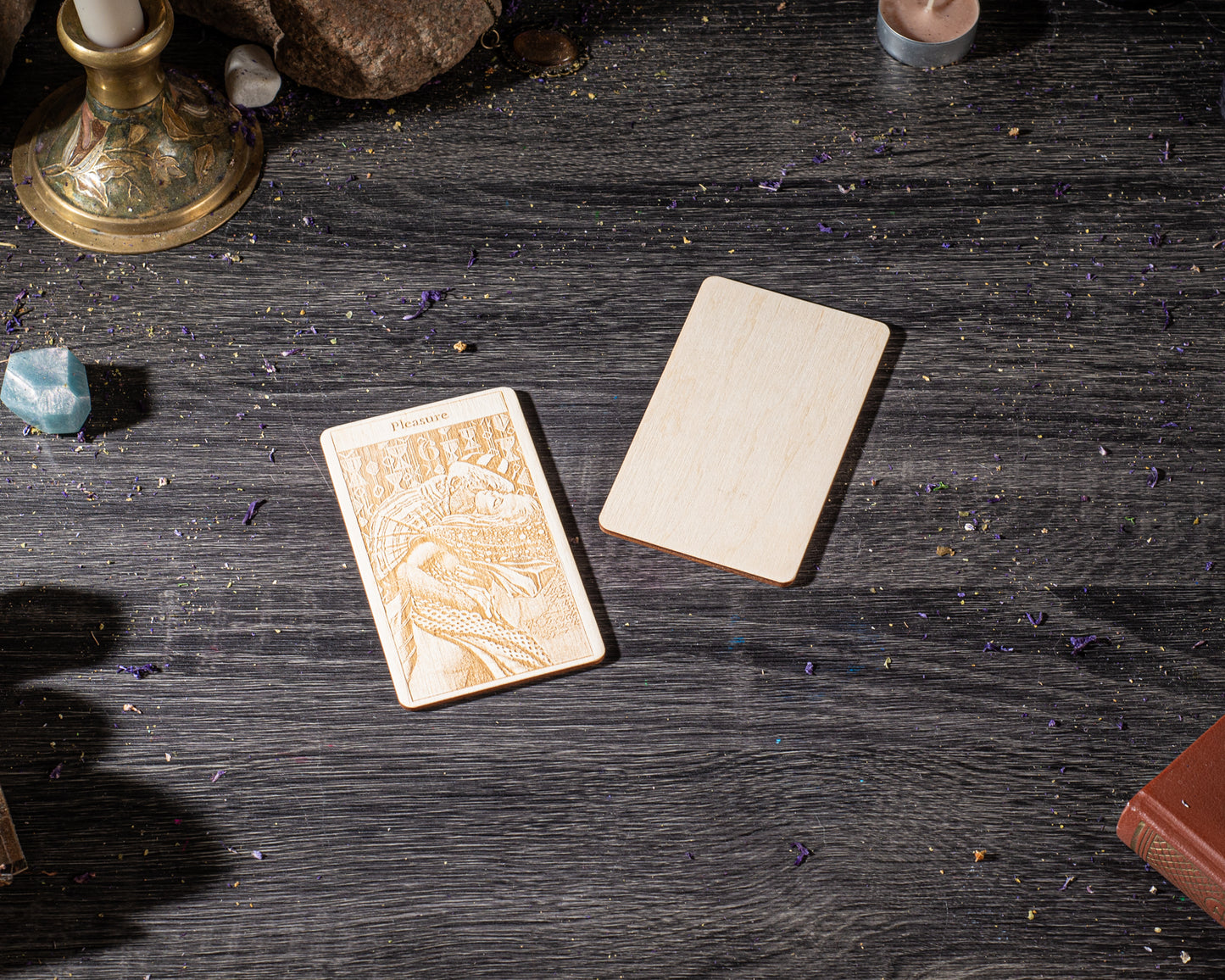 a wooden card with an embossed design, placed on a dark wooden surface alongside other objects such as a candle, a book, and some crystals.