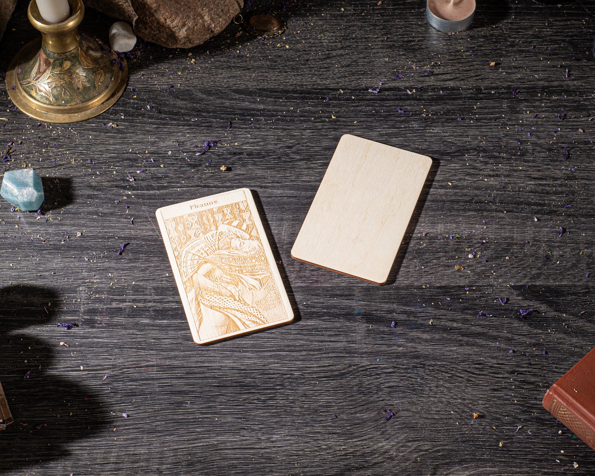 a wooden card with an embossed design, placed on a dark wooden surface alongside other objects such as a candle, a book, and some crystals.
