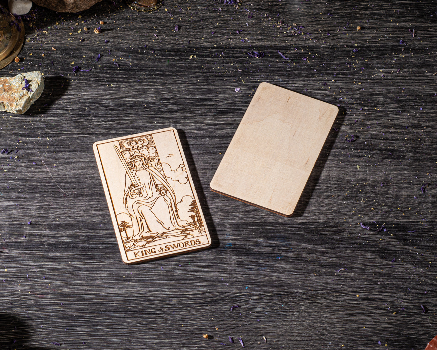 a wooden card with a design of a tarot card, specifically the King of Swords, placed on a wooden surface.