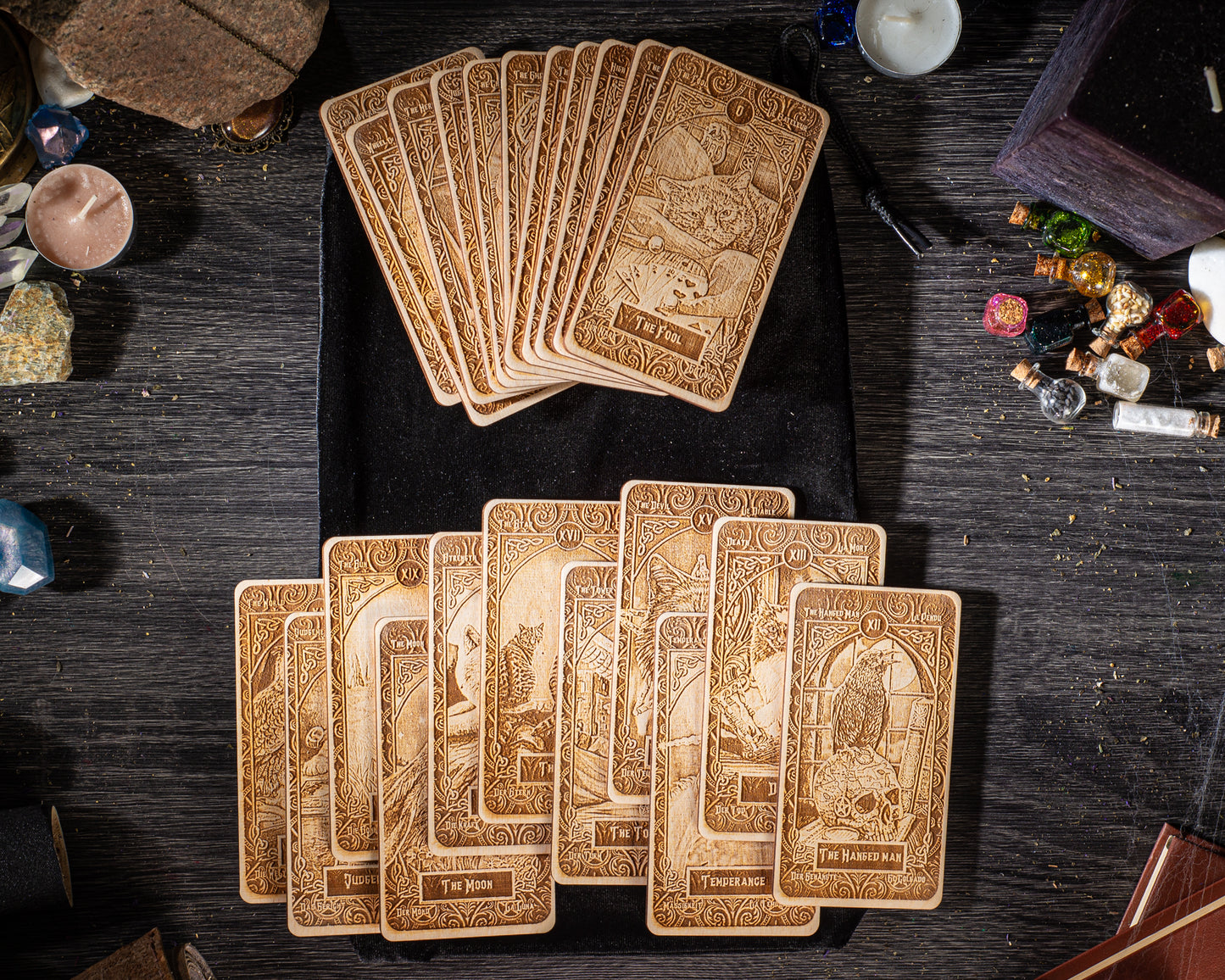 A collection of wooden tarot cards is spread out on a wooden surface, along with various other items such as candles, crystals, and small figurines.