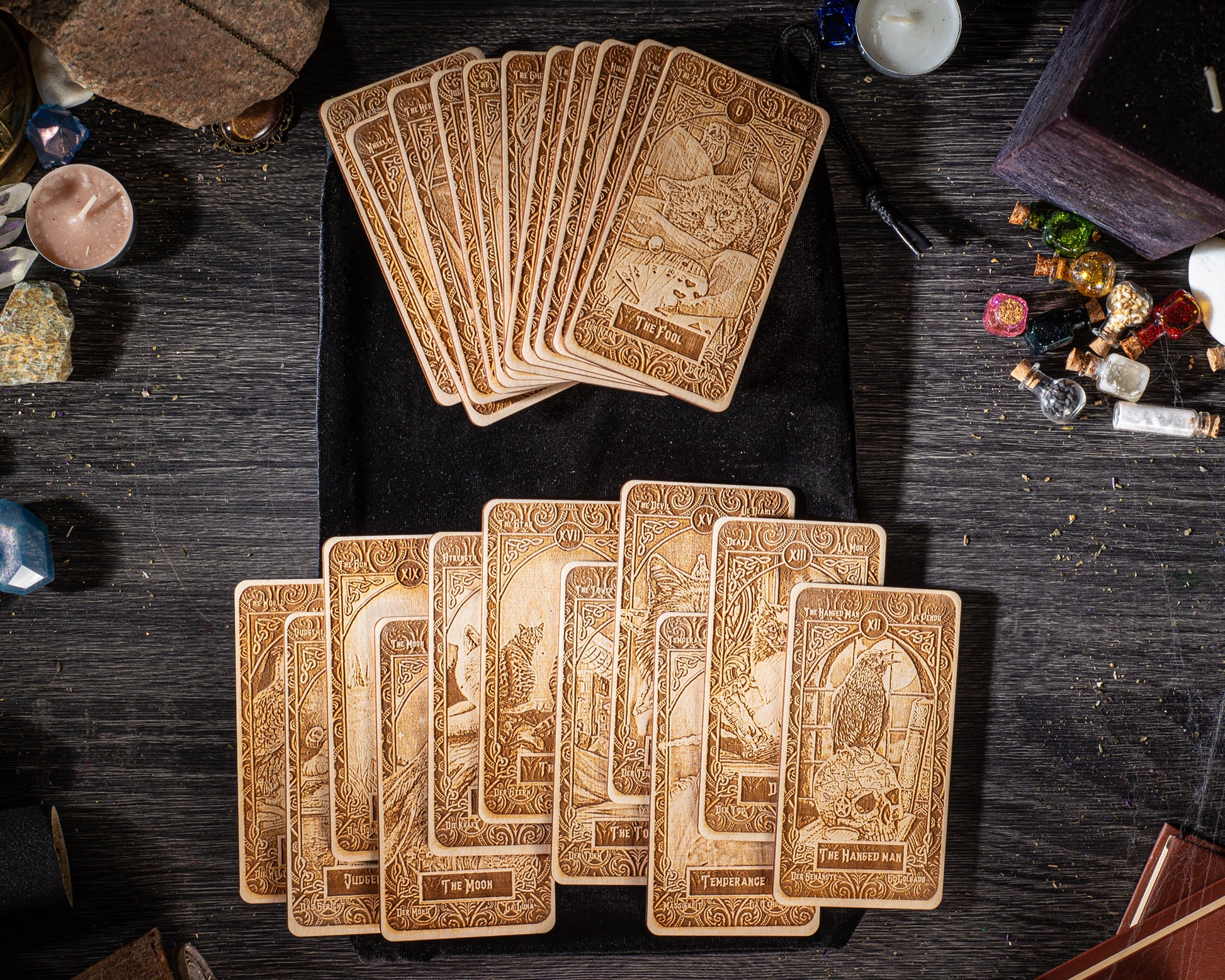 A collection of wooden tarot cards is spread out on a wooden surface, along with various other items such as candles, crystals, and small figurines.