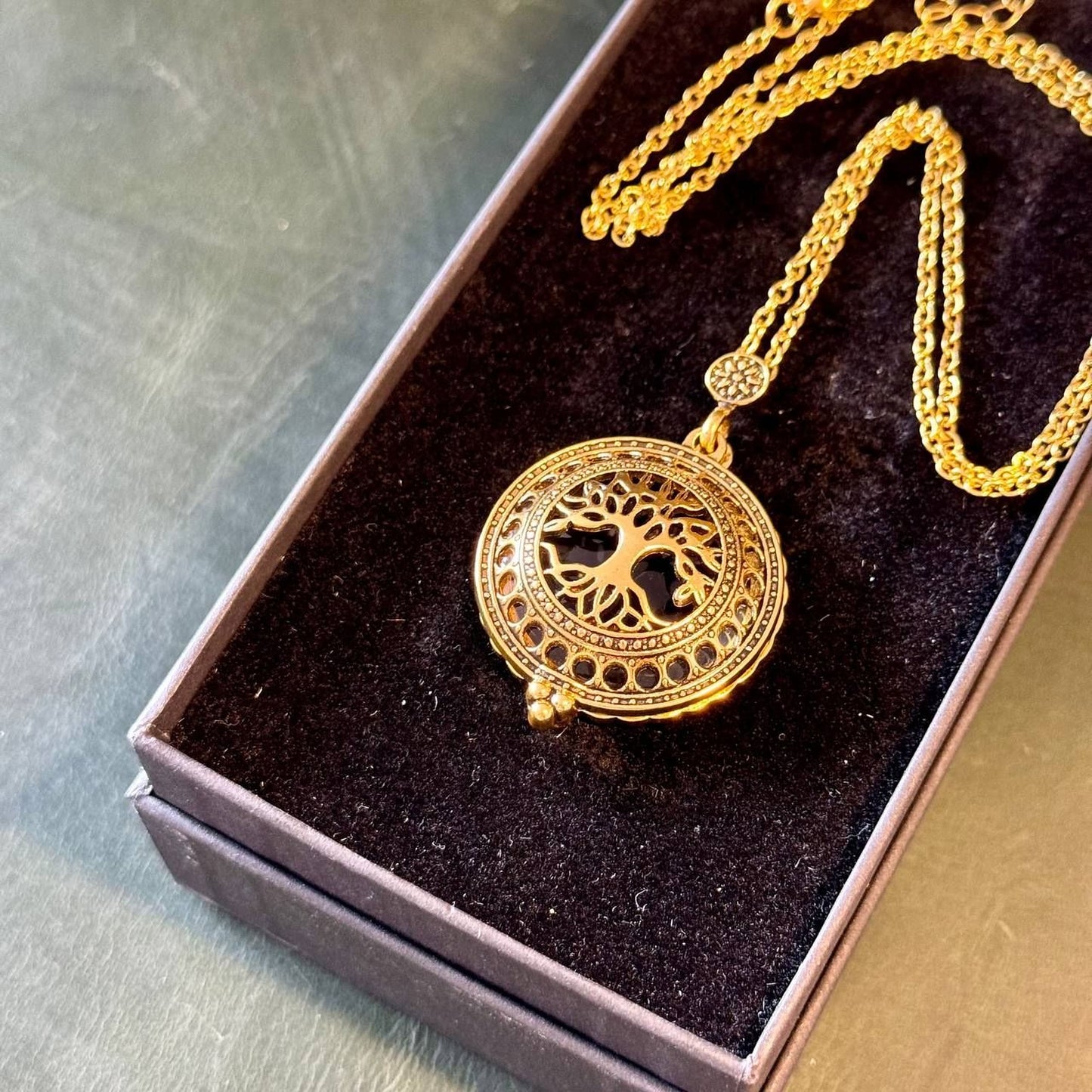 A gold-colored pendant necklace with a tree design is displayed in a black jewelry box.