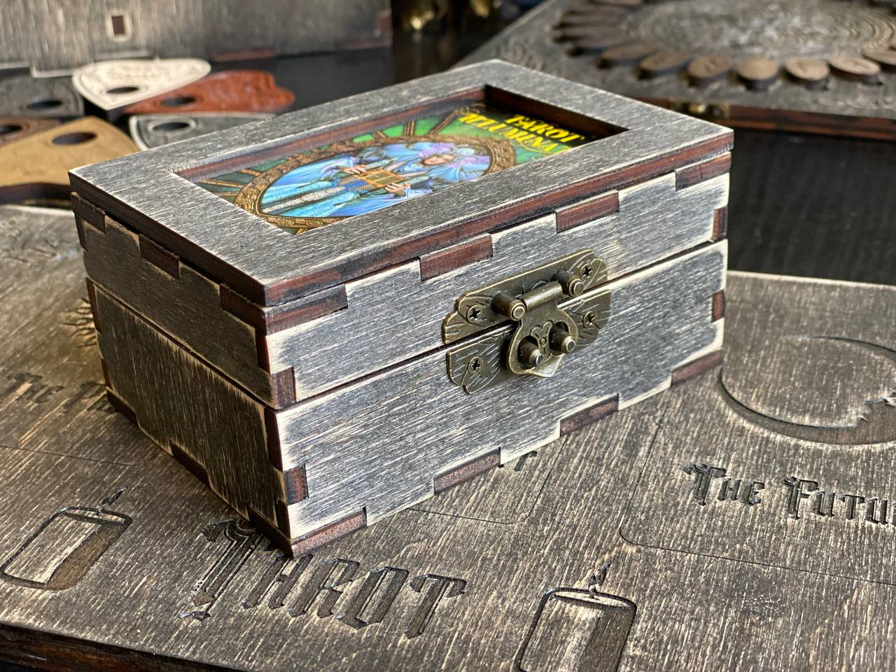 A wooden box with a metal clasp, sitting on a wooden surface with various other objects in the background.