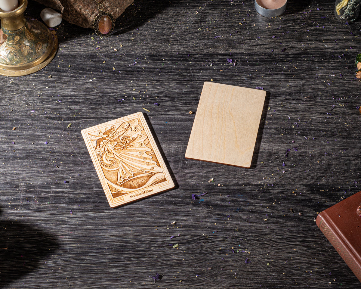 a wooden card with an intricate design, placed on a dark wooden surface alongside a wooden block and a book.