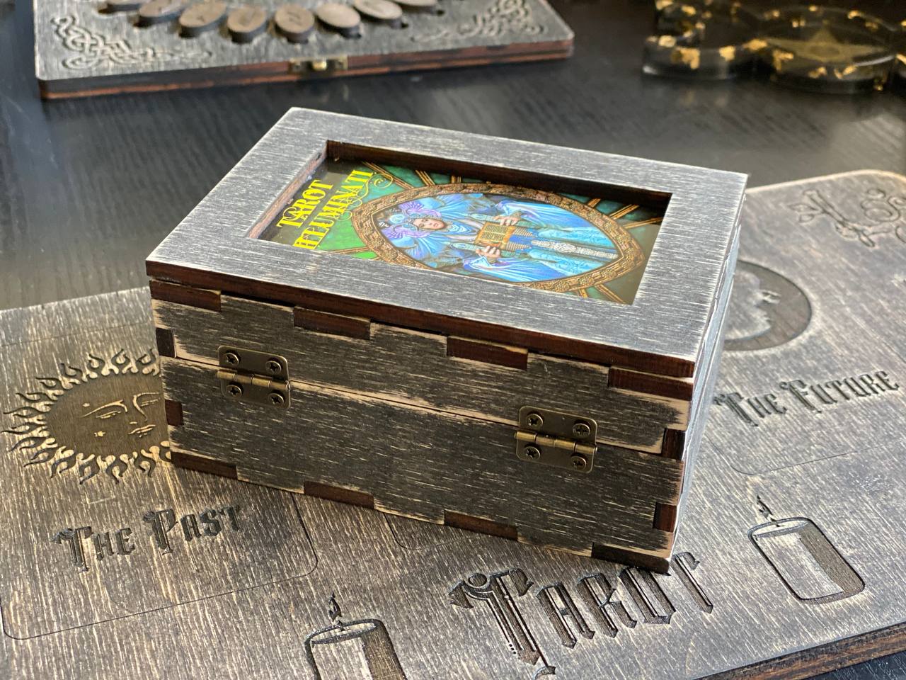 A wooden box with a lid, featuring a colorful illustration on the front, placed on a wooden surface with embossed text and designs.
