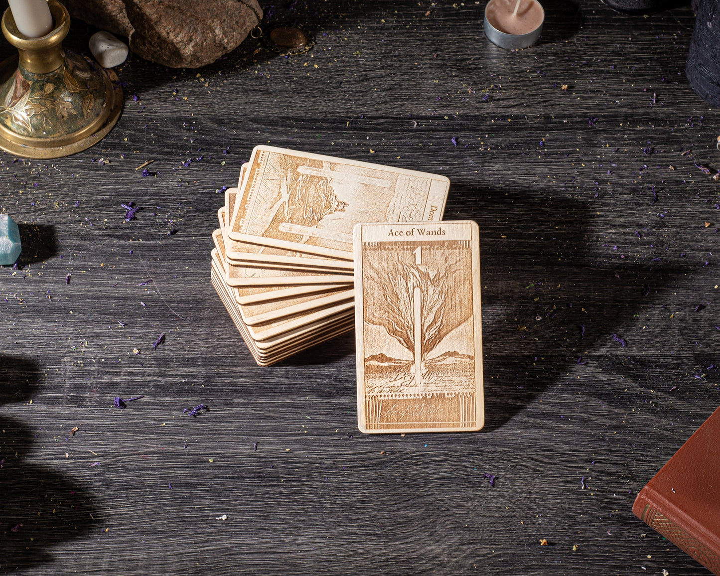 A stack of wooden tarot cards is placed on a wooden surface, with a candle and some other objects in the background.