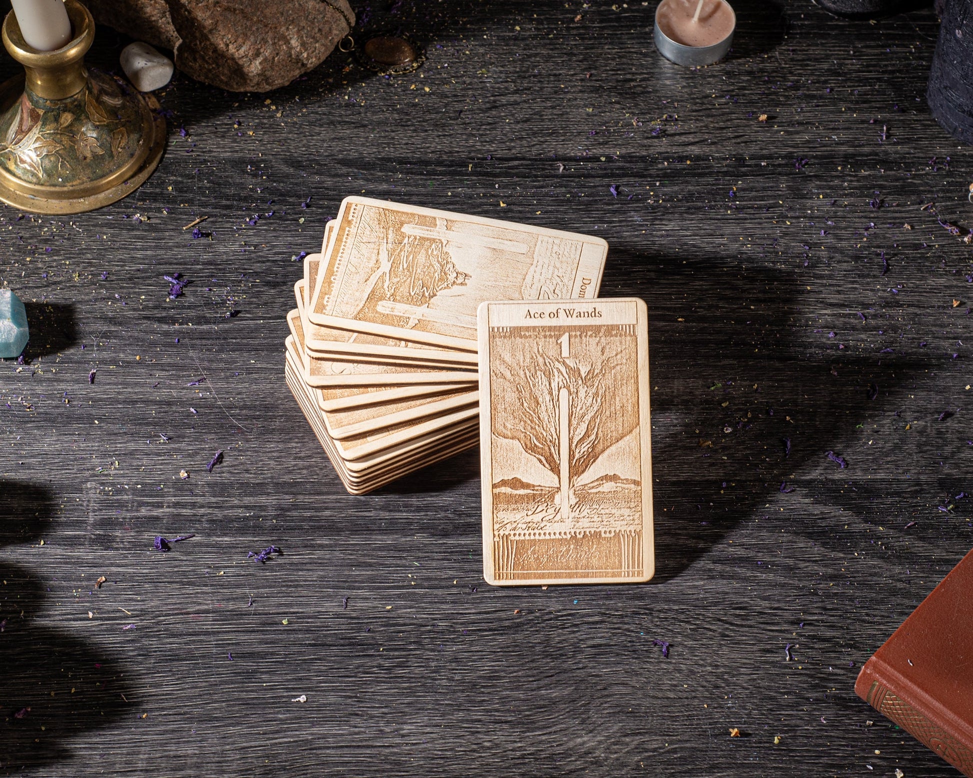 A stack of wooden tarot cards is placed on a wooden surface, with a candle and some other objects in the background.
