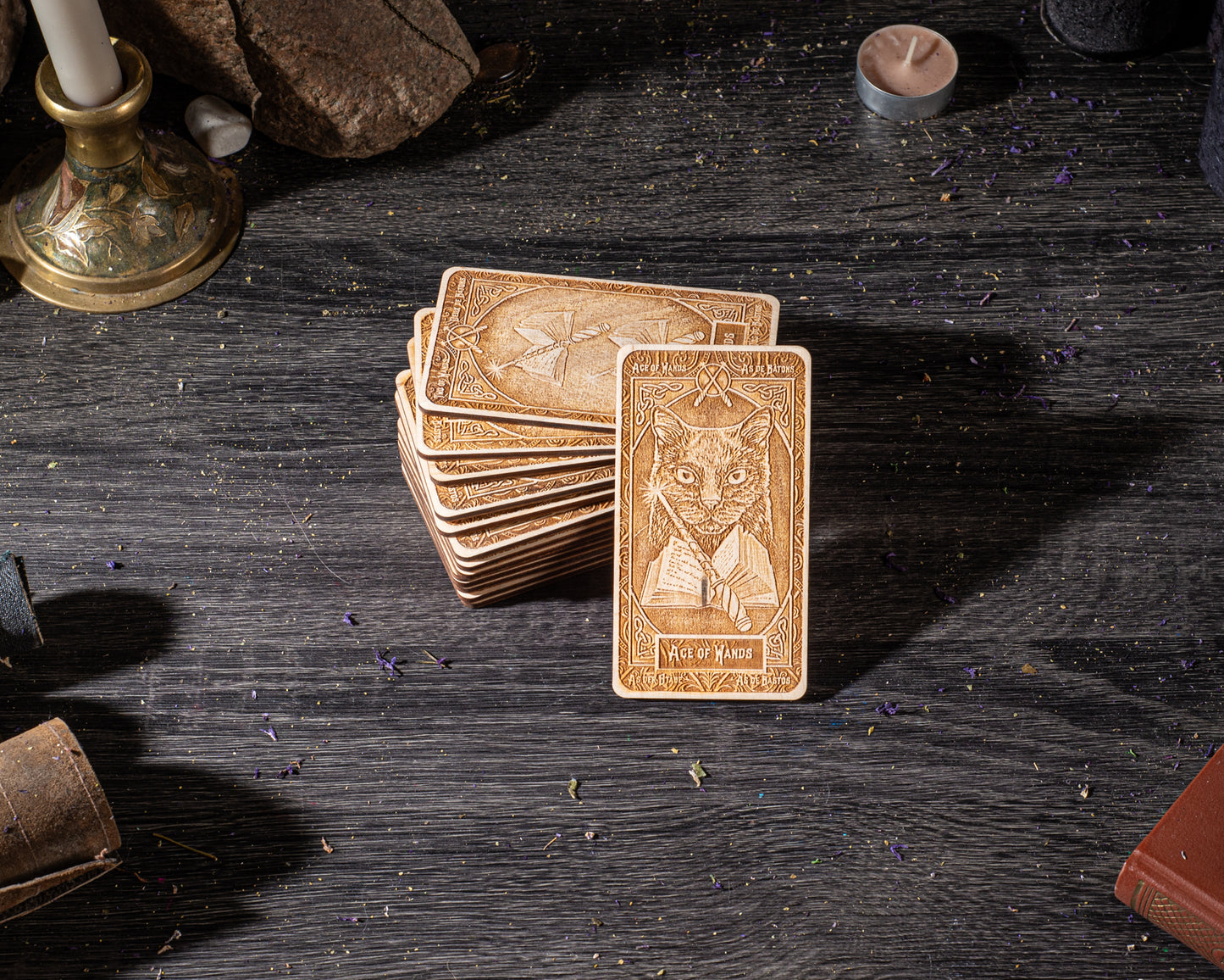 a stack of wooden cards with intricate designs, including a prominent card with a cat illustration, placed on a dark wooden surface.