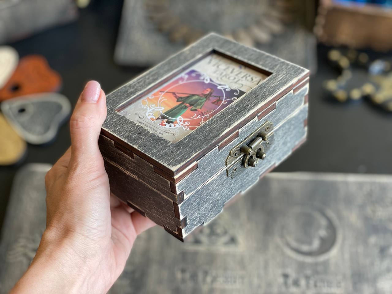 A hand is holding a small wooden box with a colorful design on the front.
