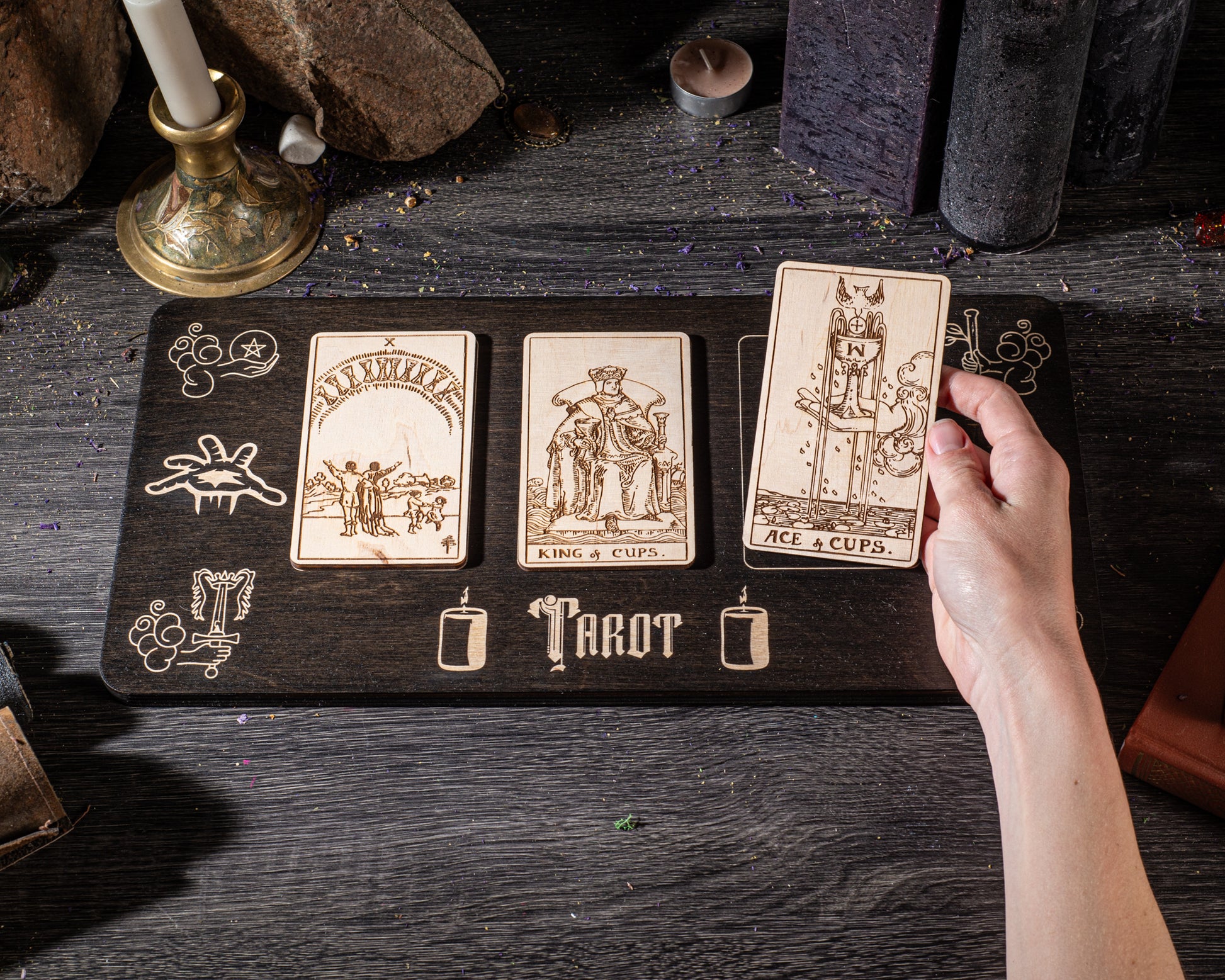 A hand is holding a wooden board with three tarot cards on it, arranged in a row.