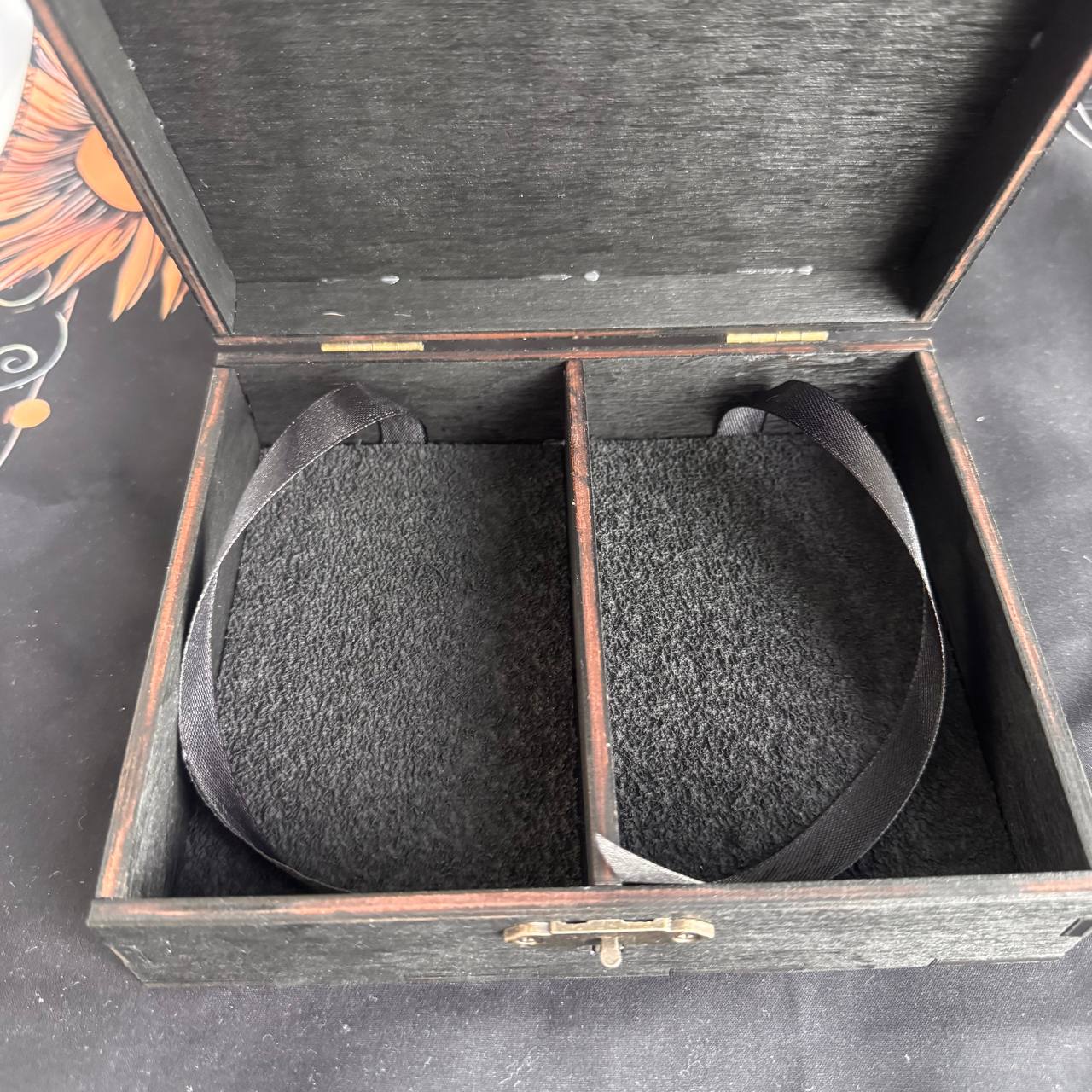 An open wooden box with a black interior, containing two black straps.