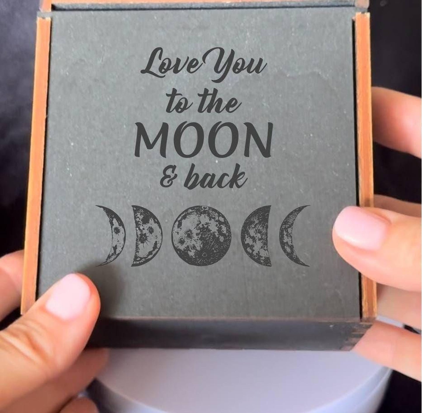 A person's hands holding a black box with a gray background and the text "Love You to the MOON & back" printed on it.