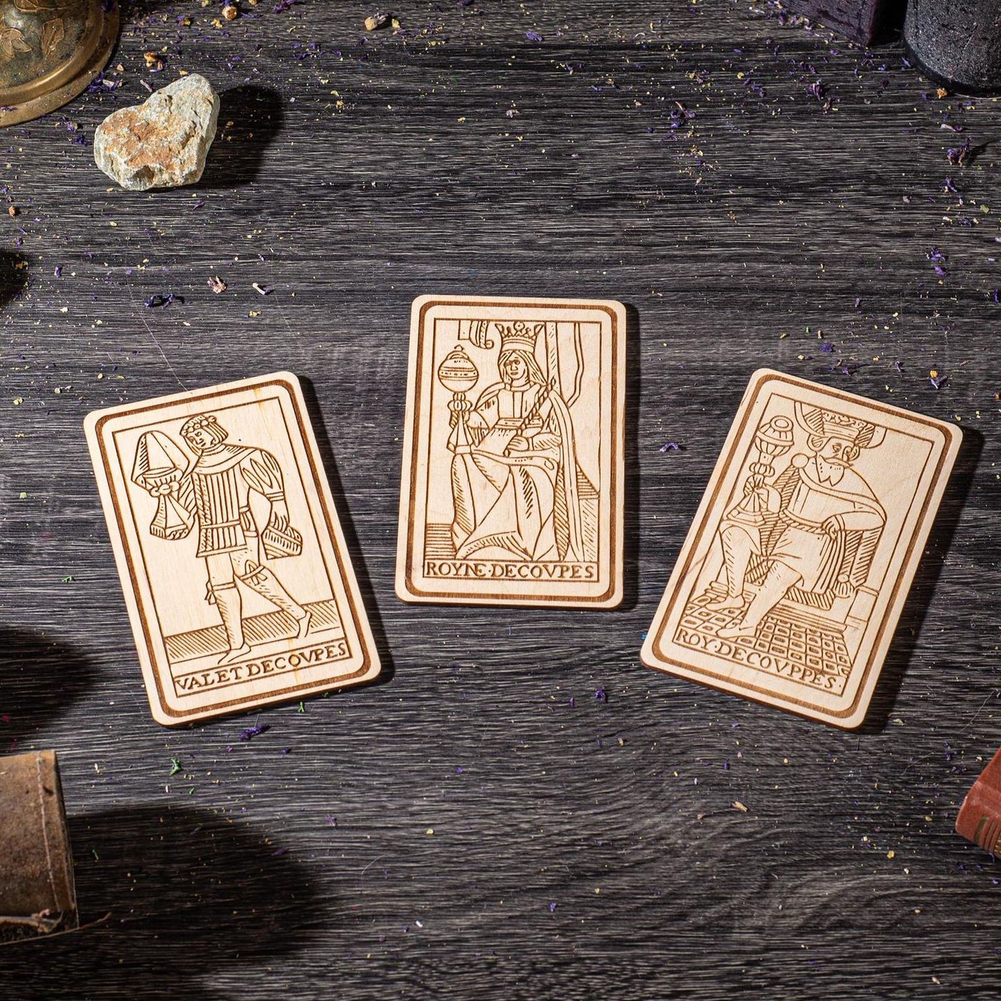 Three wooden tarot cards are displayed on a wooden surface, each depicting a different card with its own unique illustration.
