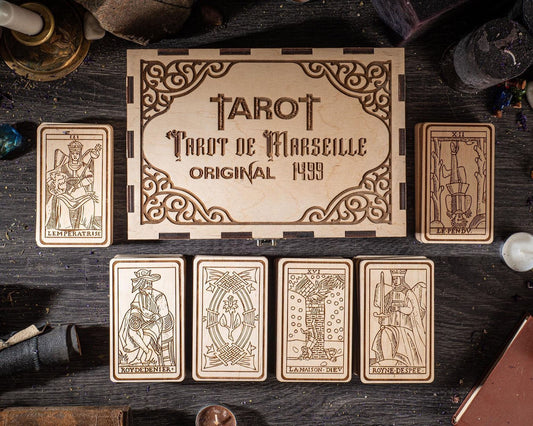 a wooden box with the text "TAROT" and "Tarot de Marseille Original 1949" on it, along with six tarot cards arranged below it.