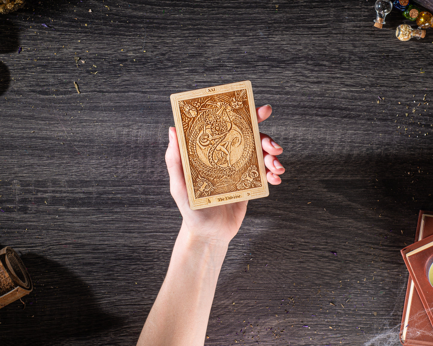 A hand holding a wooden tarot card with intricate designs on a dark wooden surface.