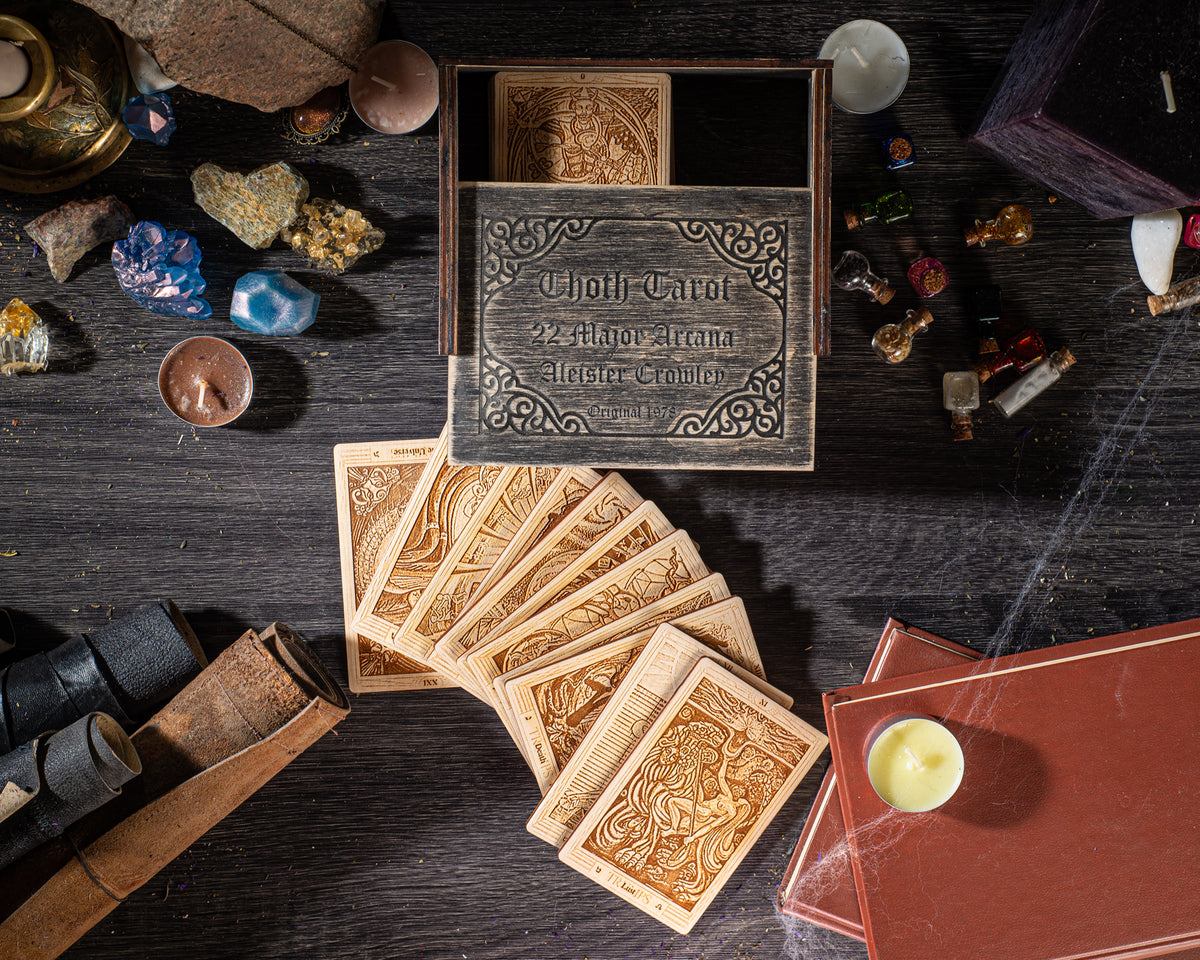a collection of various objects, including a wooden box with ornate designs, playing cards, candles, and other items, all arranged on a dark wooden surface.