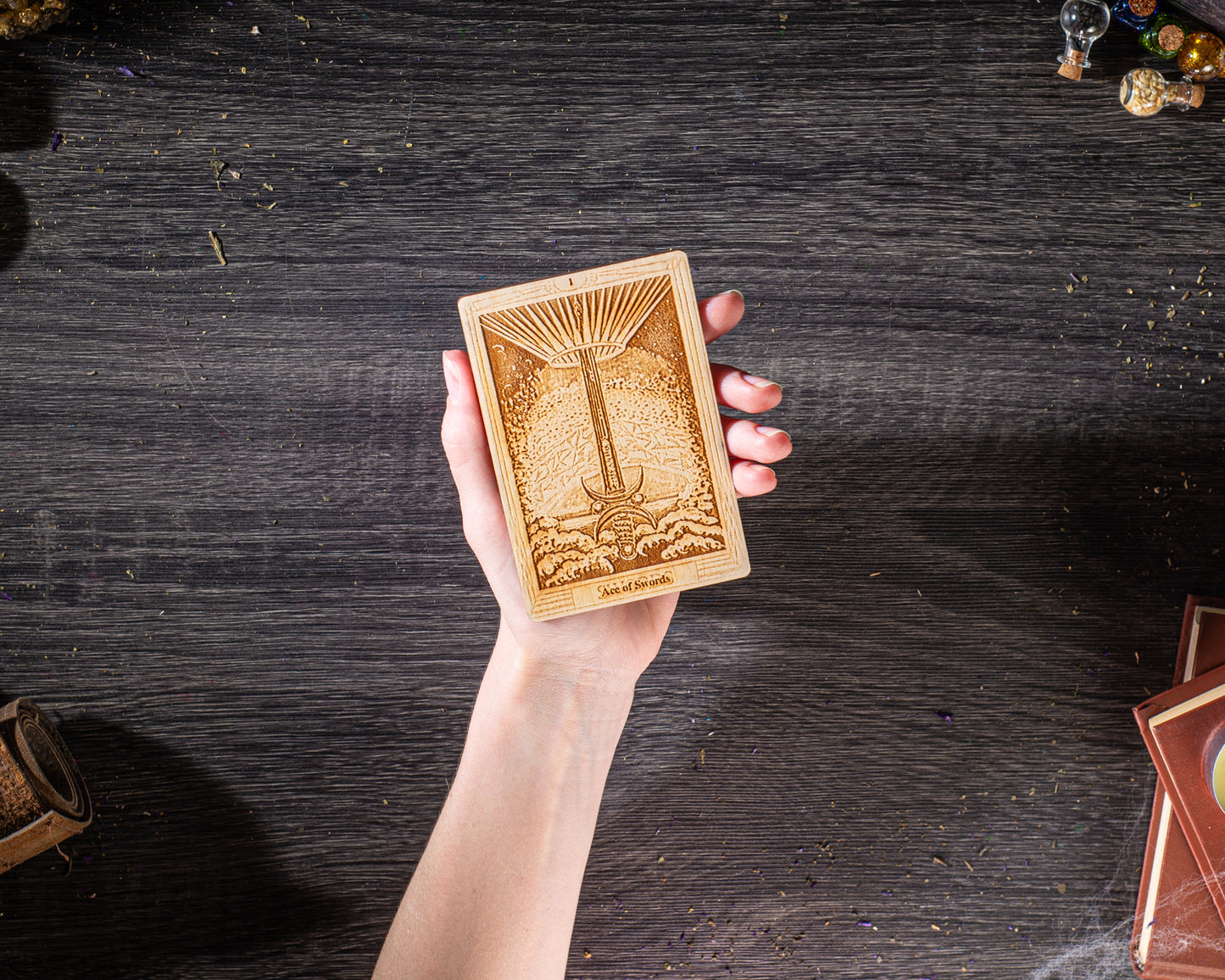 A hand holding a wooden tarot card with an intricate design on a dark wooden surface.