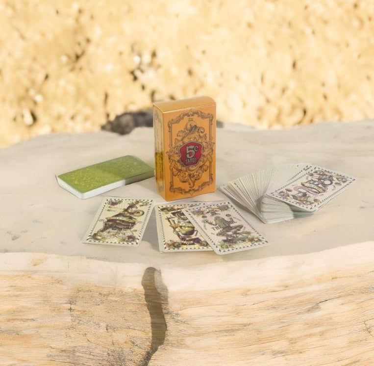a deck of playing cards, a tarot card box, and a green rectangular object on a wooden surface.