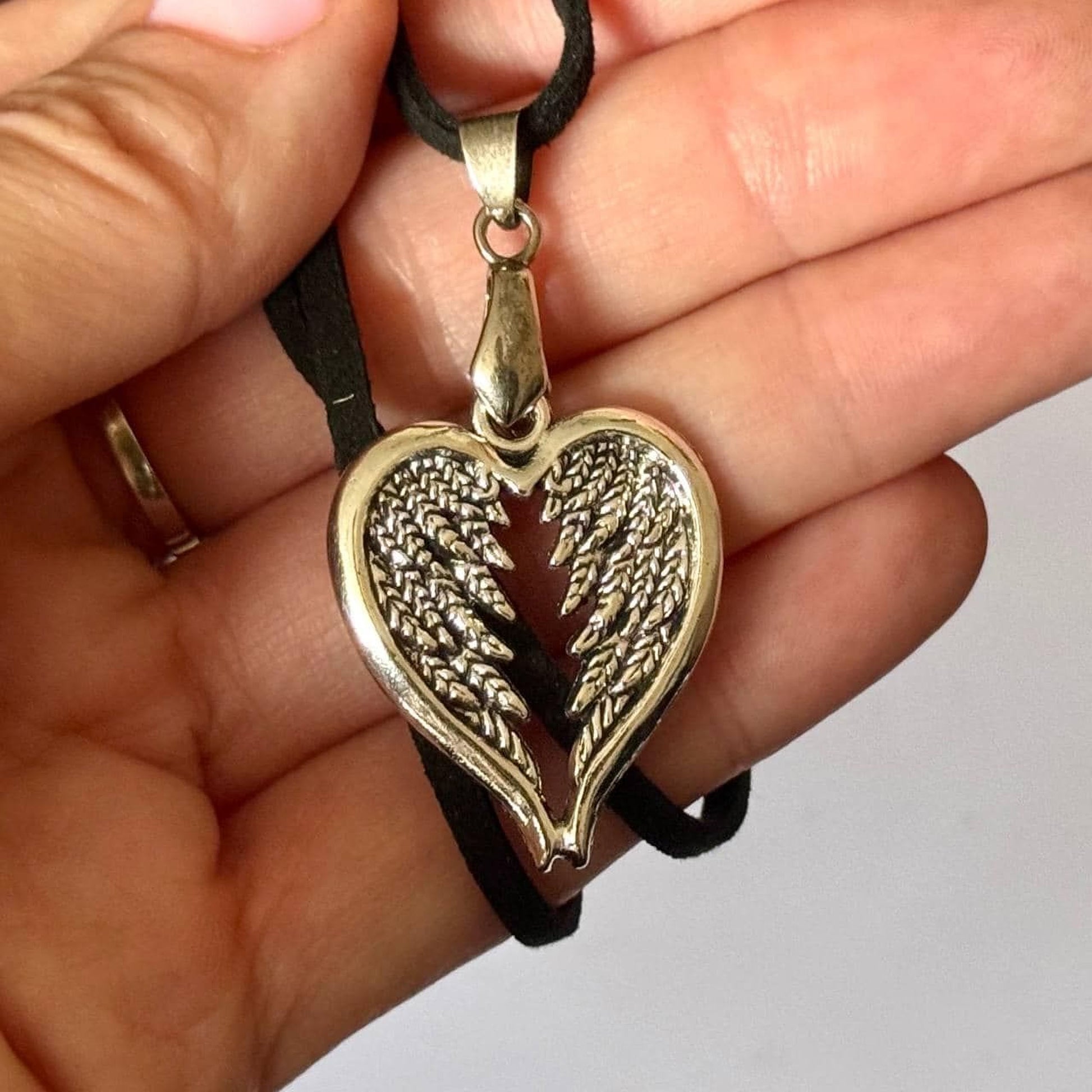 A hand holding a heart-shaped pendant with wing-like designs.