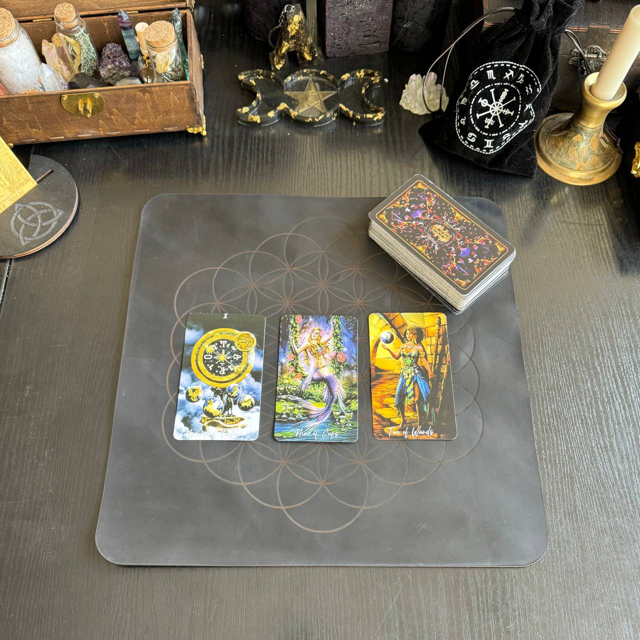 a tarot card spread on a wooden surface, with three cards arranged in a row. The cards feature various designs and illustrations, suggesting a tarot card reading setup.