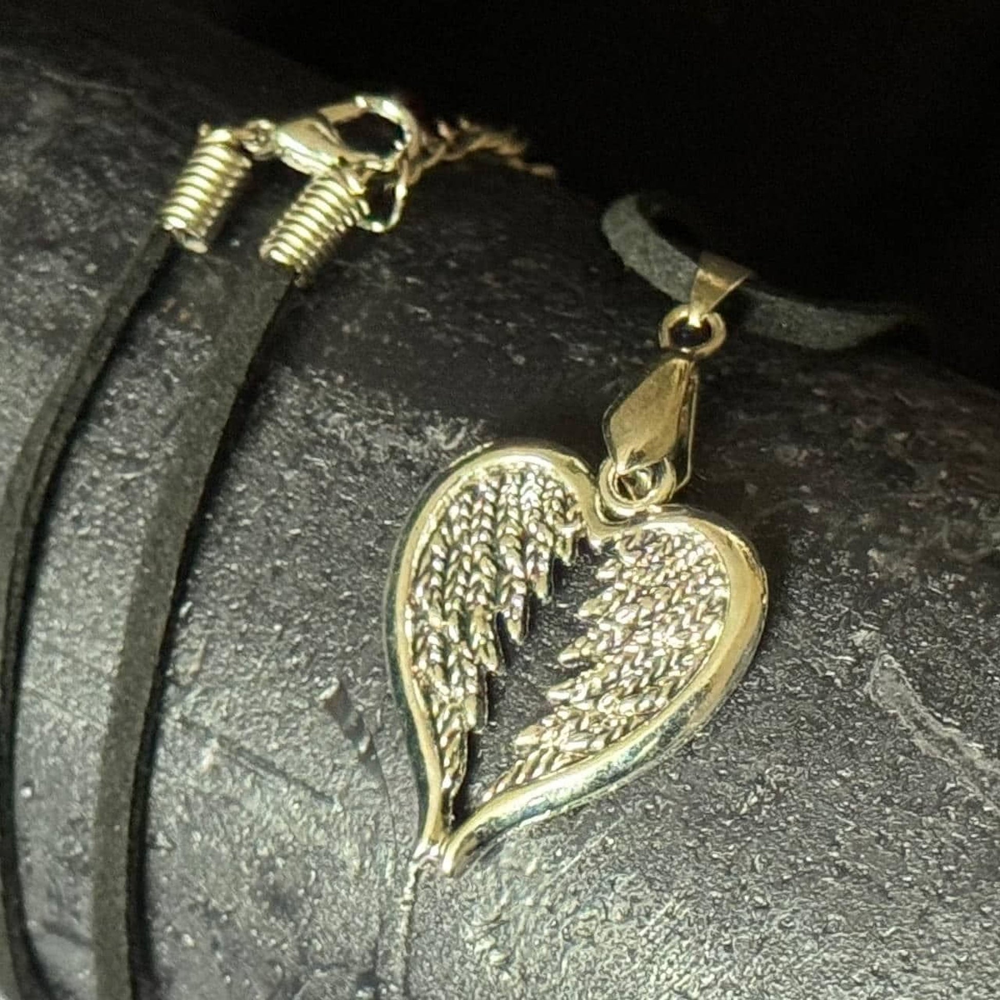A heart-shaped pendant with a metallic, winged design is displayed on a black surface.