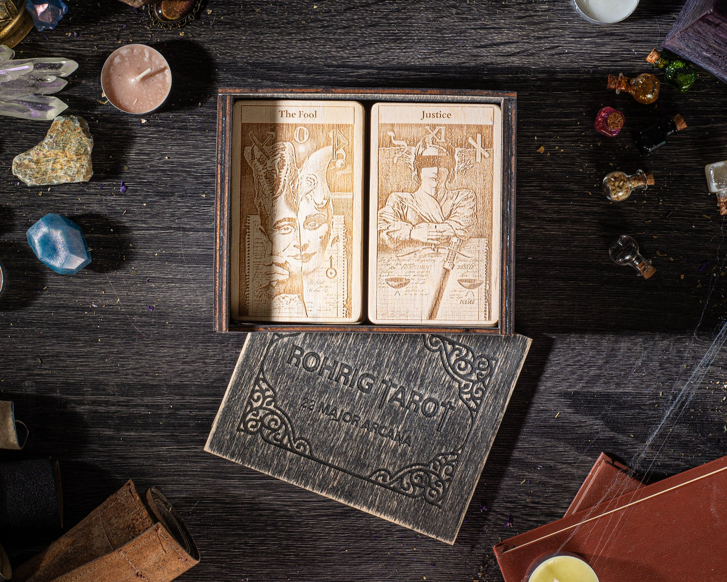 a wooden box with two tarot cards inside, along with various objects such as candles, crystals, and books scattered around.