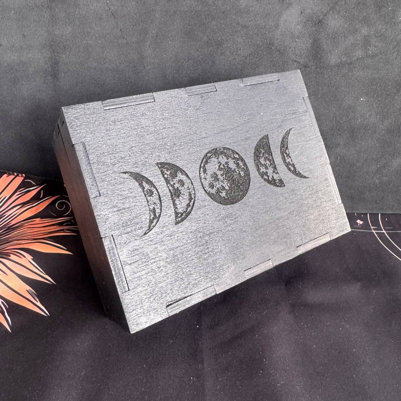 A metallic box with the phases of the moon printed on it, sitting on a dark surface.