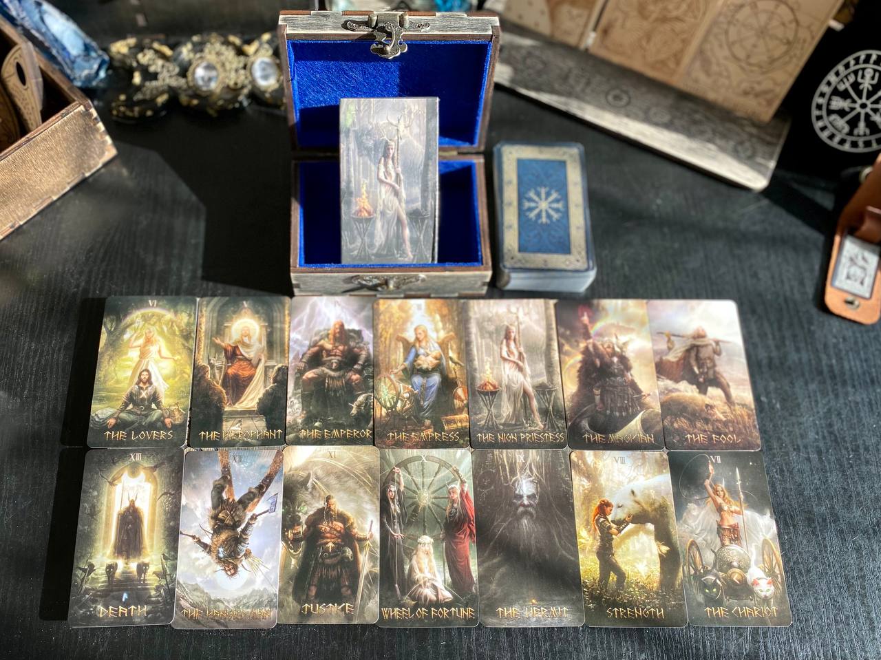 a collection of tarot cards arranged on a table, with a blue-opened box containing additional cards and a deck of playing cards visible.