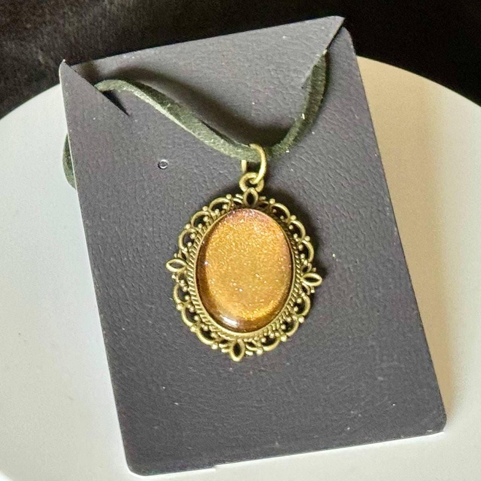 A gold-colored pendant with a decorative frame is displayed on a black card or card holder.