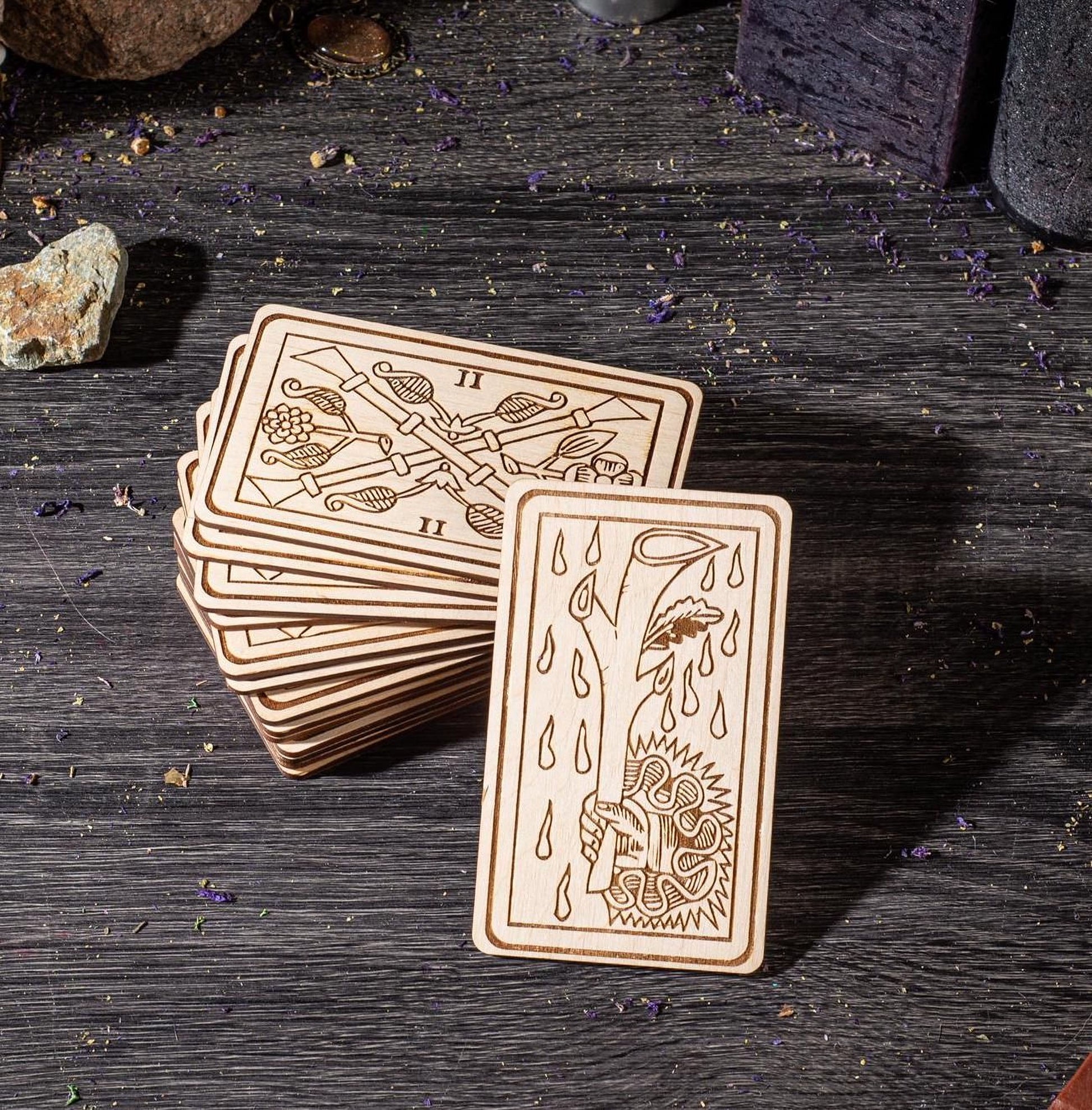 A stack of wooden cards with intricate designs on them, placed on a wooden surface with scattered purple objects around.