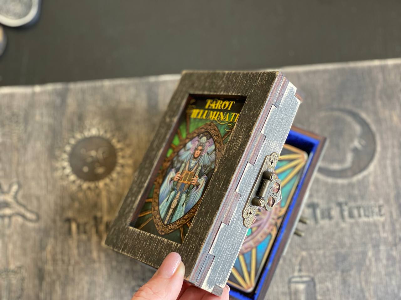 A hand is holding a small wooden box with a tarot card visible inside.