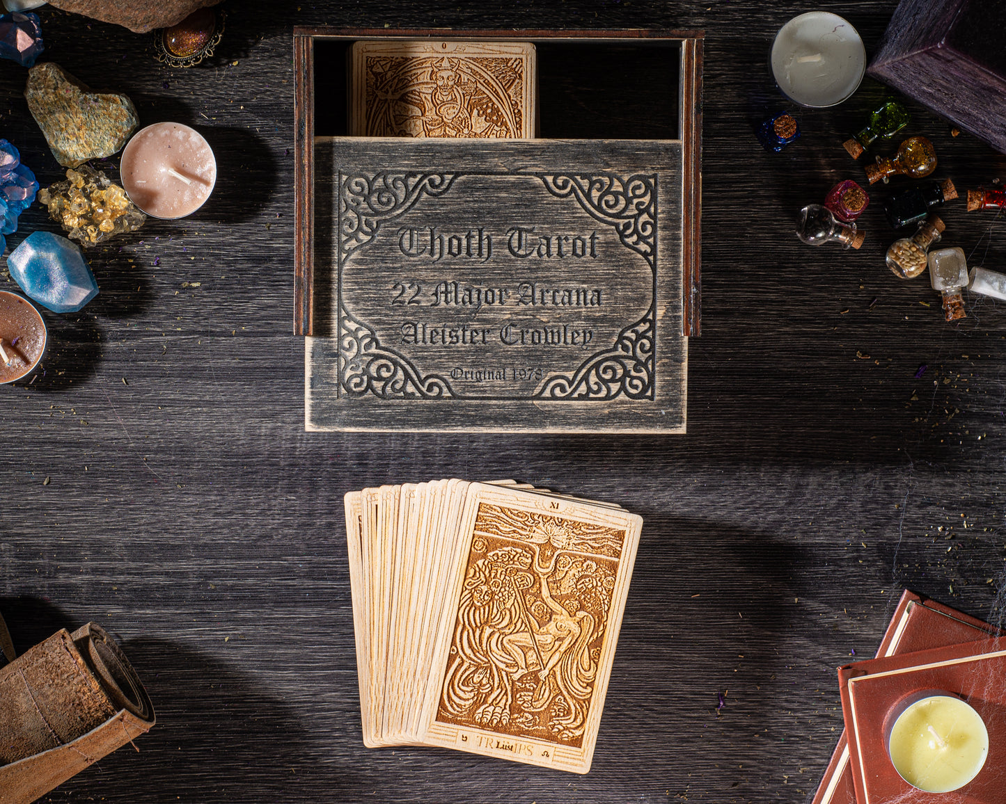 a wooden box with a label, a deck of playing cards, and various objects such as candles and crystals arranged on a wooden surface.