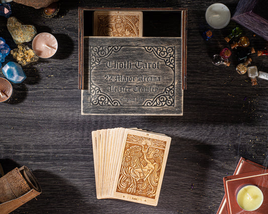 a wooden box with a label, a deck of playing cards, and various objects such as candles and crystals arranged on a wooden surface.