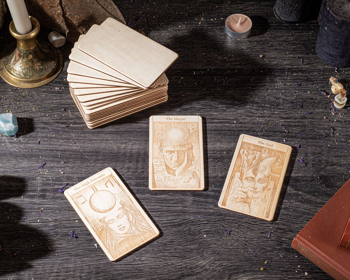 three wooden tarot cards with intricate designs, placed on a dark wooden surface alongside various objects such as candles, crystals, and books.