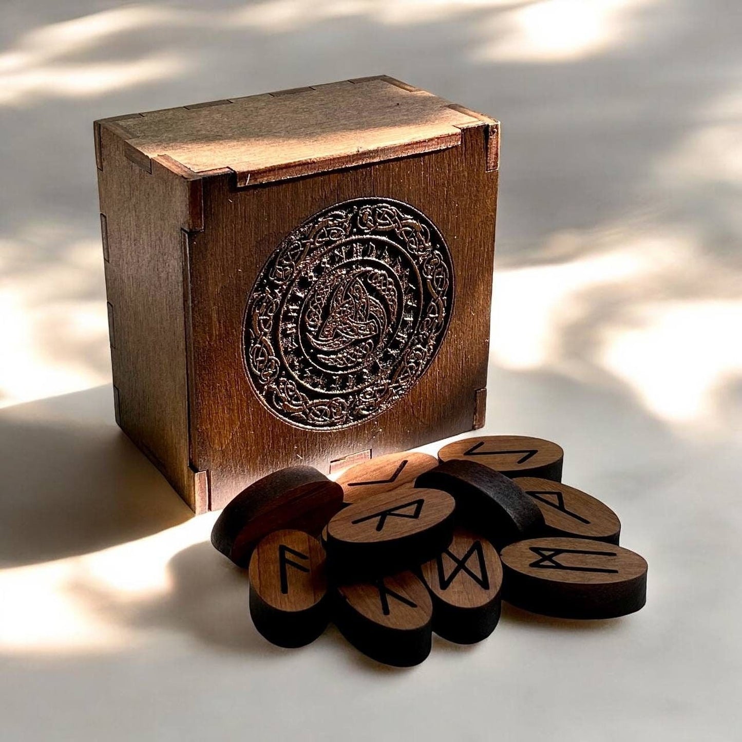 A wooden box with a decorative metal emblem and a pile of wooden blocks with carved symbols on them are placed on a white surface.