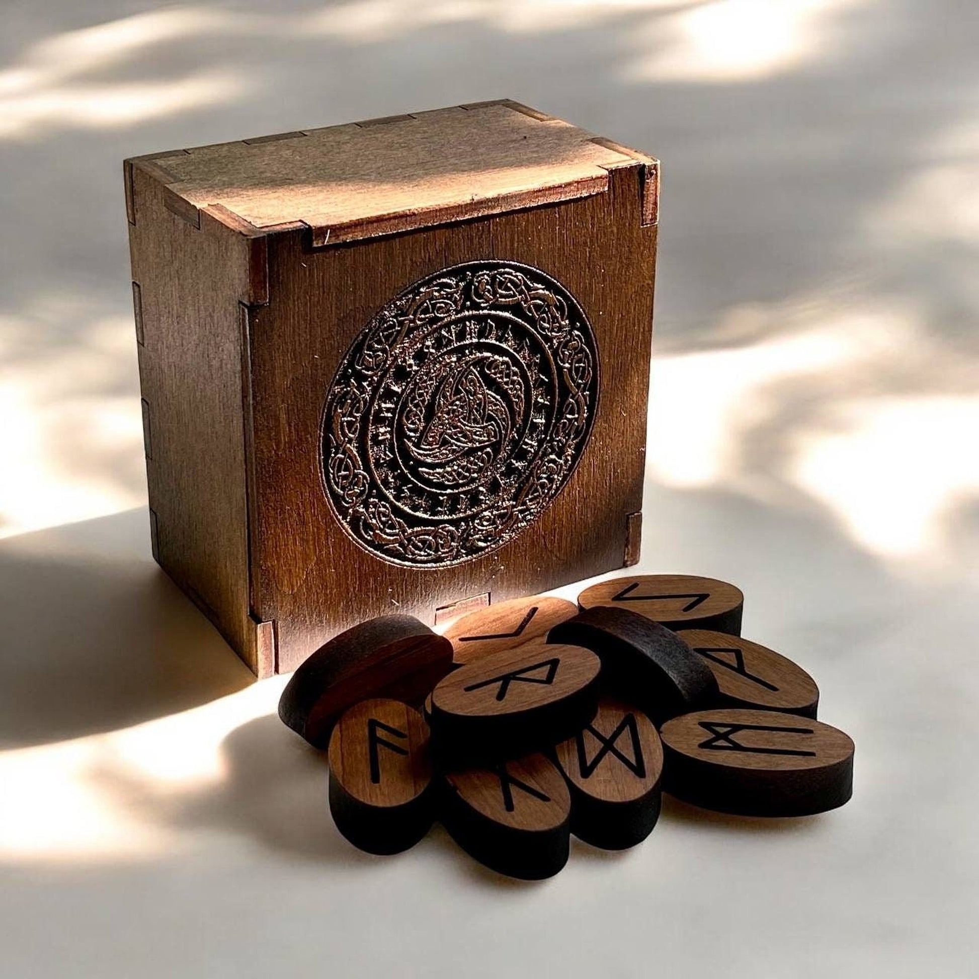 A wooden box with a decorative metal emblem and a pile of wooden blocks with carved symbols on them are placed on a white surface.