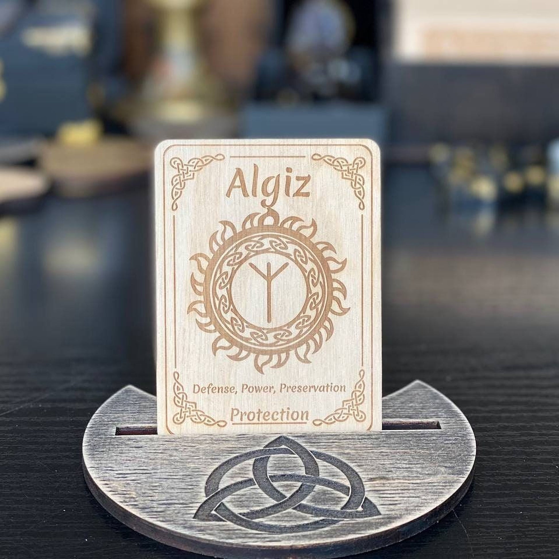A wooden card stand displaying a wooden card with the name Algiz and a symbol, placed on a wooden surface.
