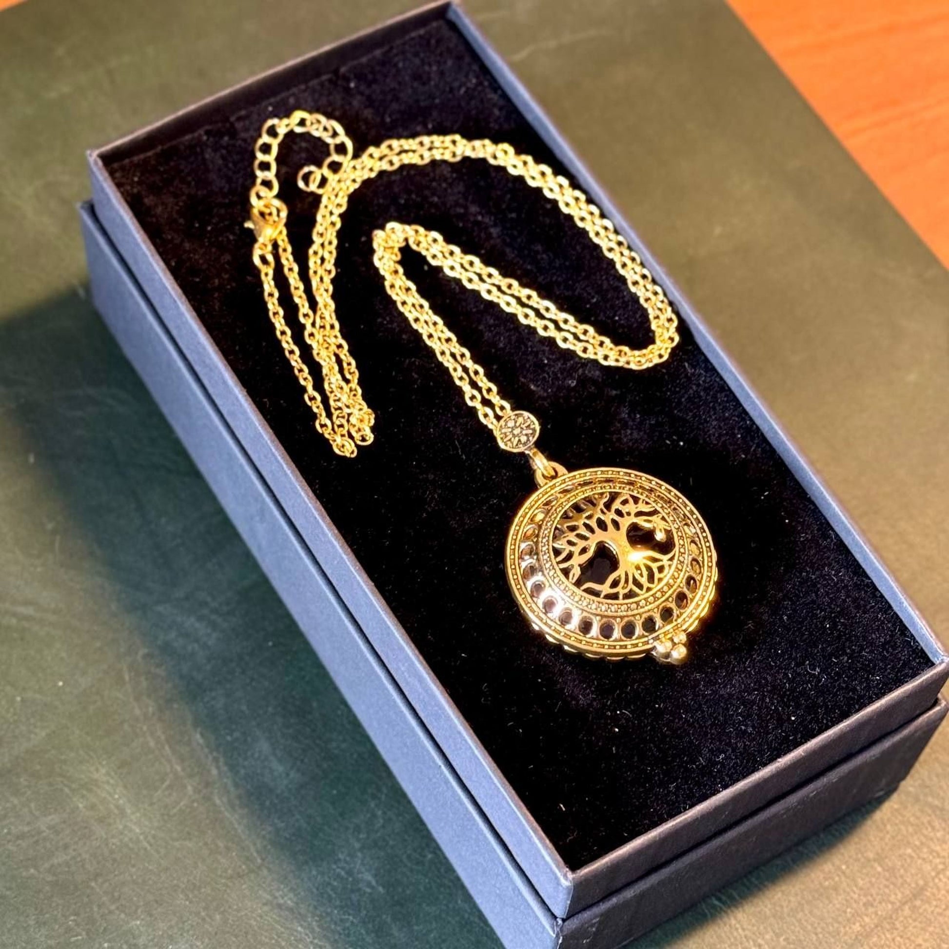 A gold-colored necklace with a pendant in the shape of a tree is displayed in a black jewelry box.