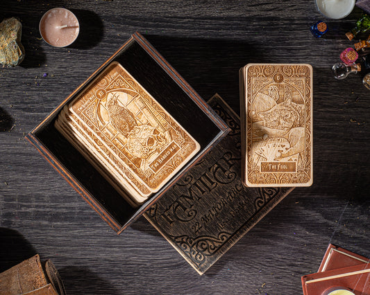 a wooden box containing several tarot cards, along with a book titled "The Family of Cards" on a wooden surface.