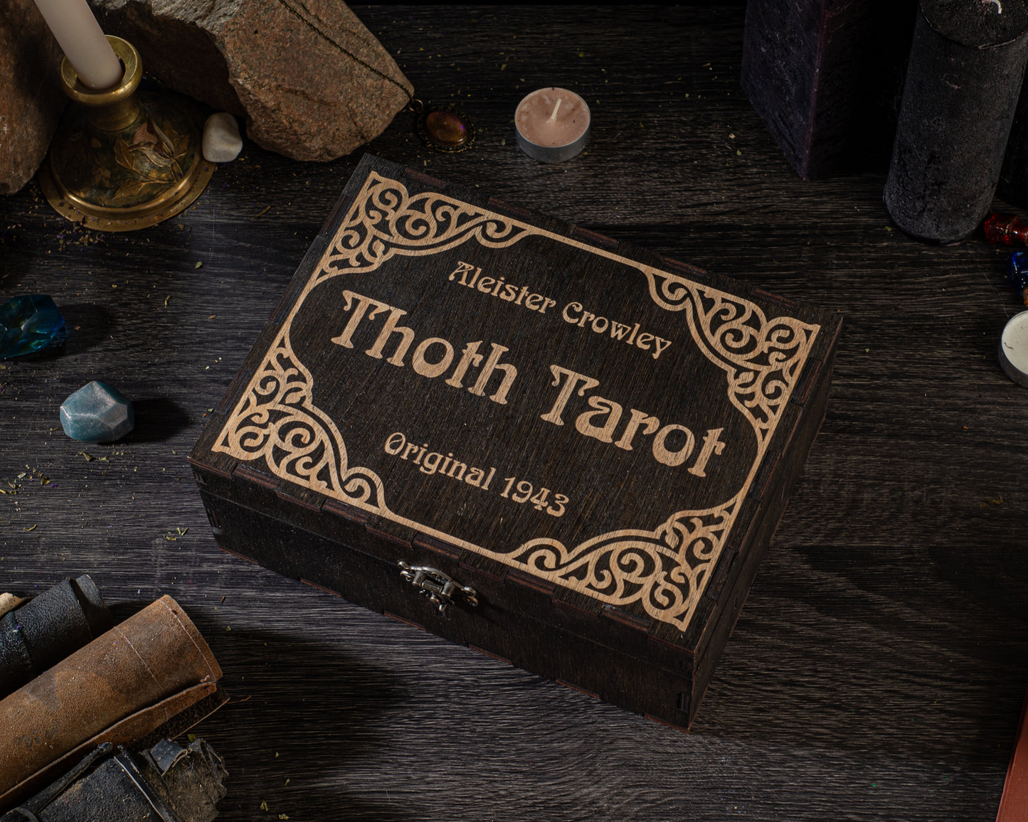A wooden box with a decorative border, labeled "Thoth Tarot" and "Original 1943", sits on a dark wooden surface surrounded by various objects.