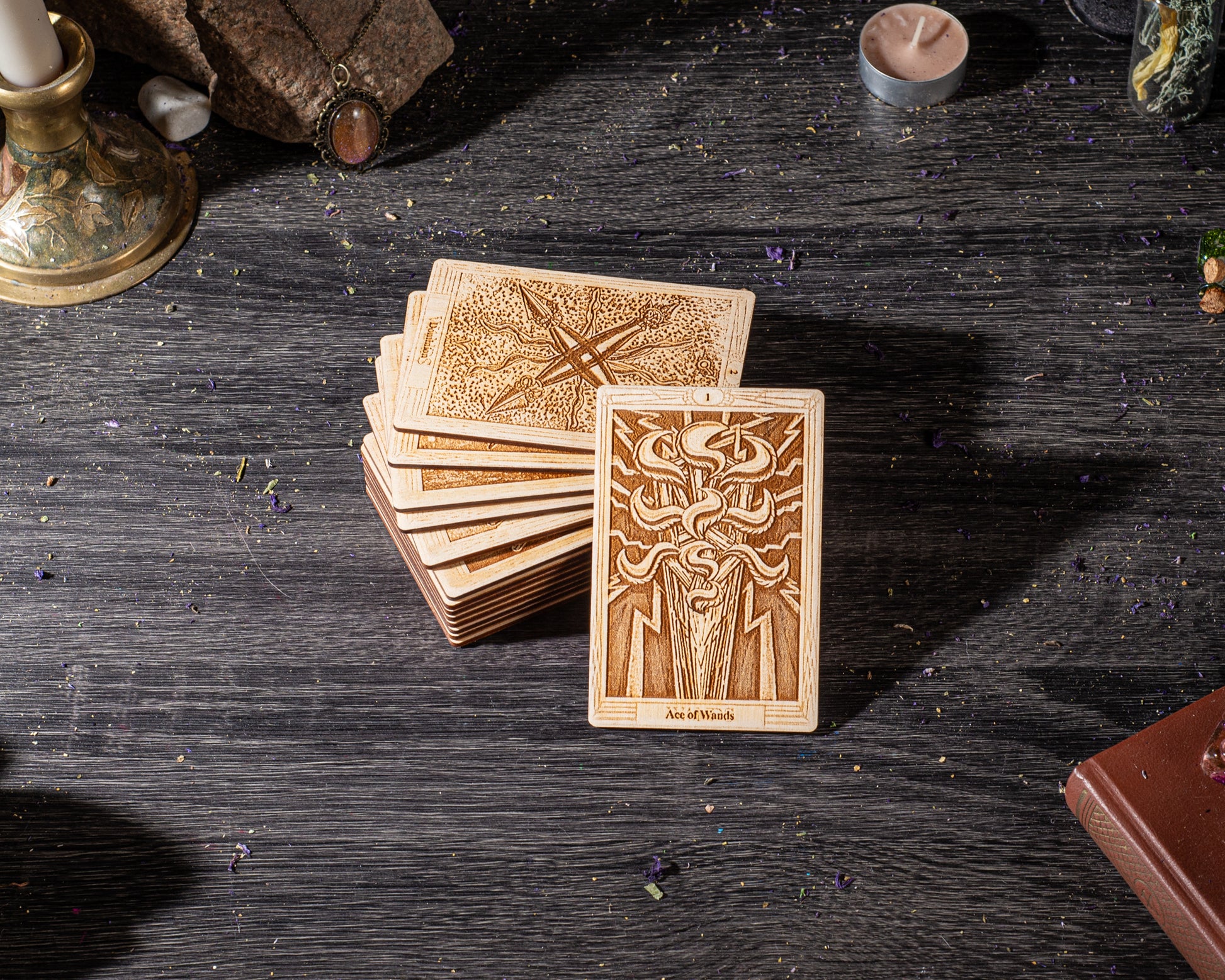 a stack of wooden tarot cards on a dark wooden surface, with a candle and other objects in the background.