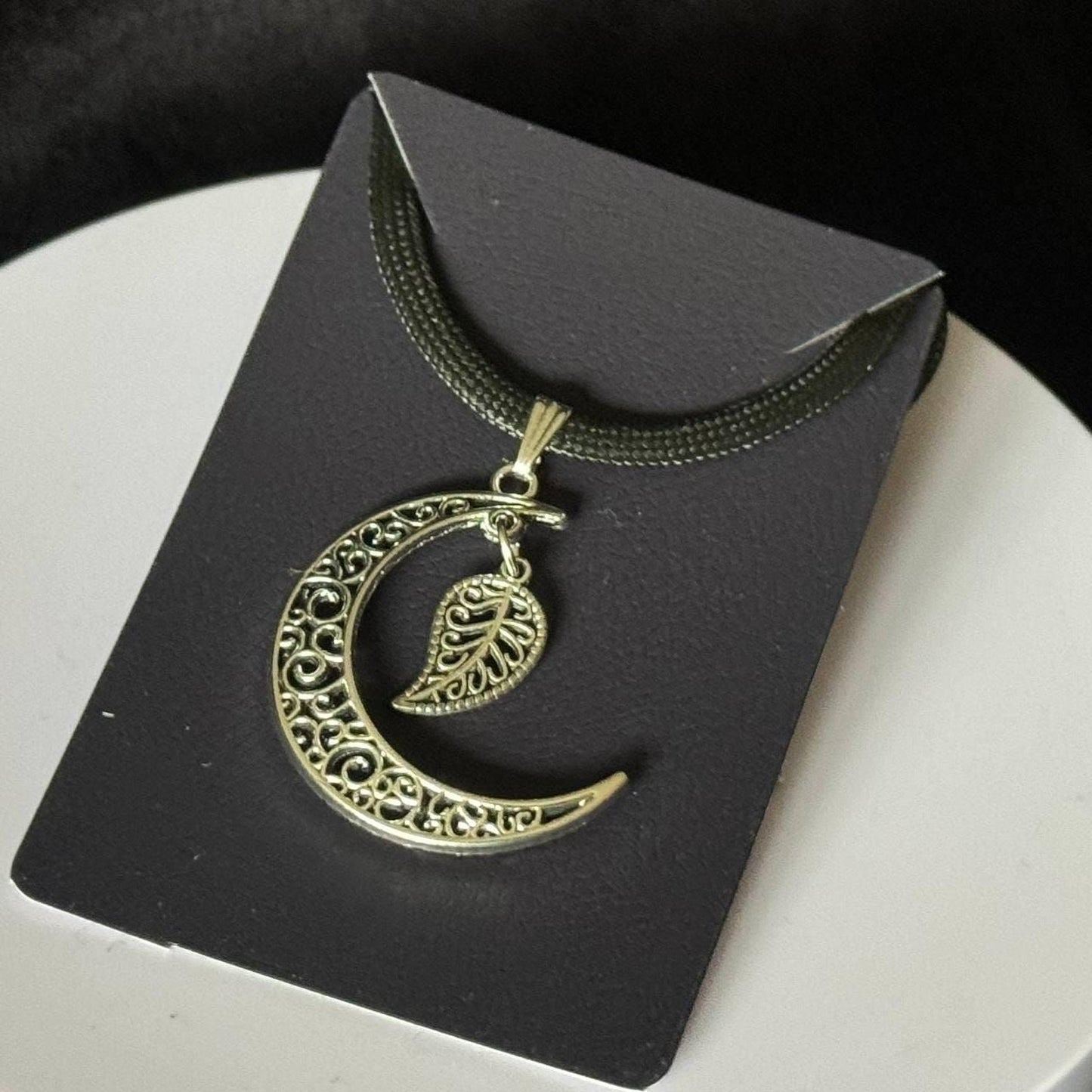 A necklace with a pendant in the shape of a crescent moon and a leaf.