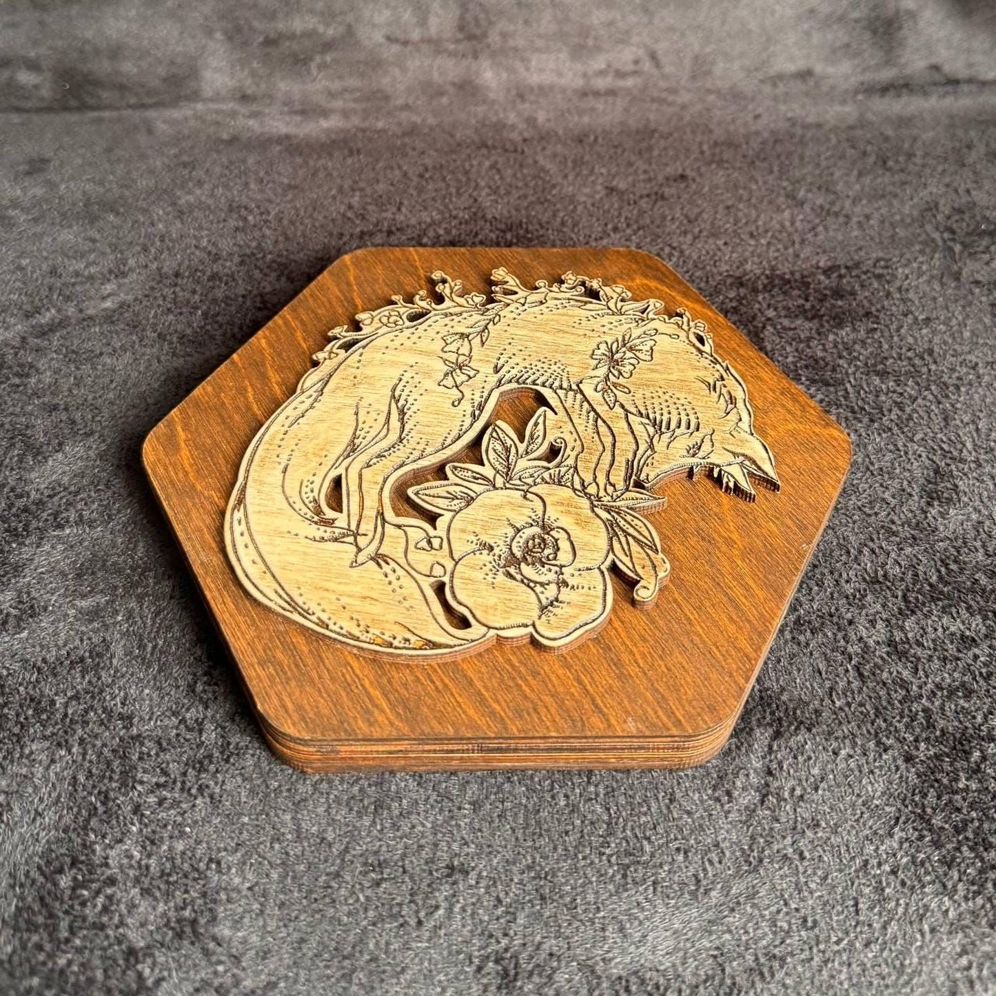 a wooden hexagonal base with a carved design depicting a fox and a flower.