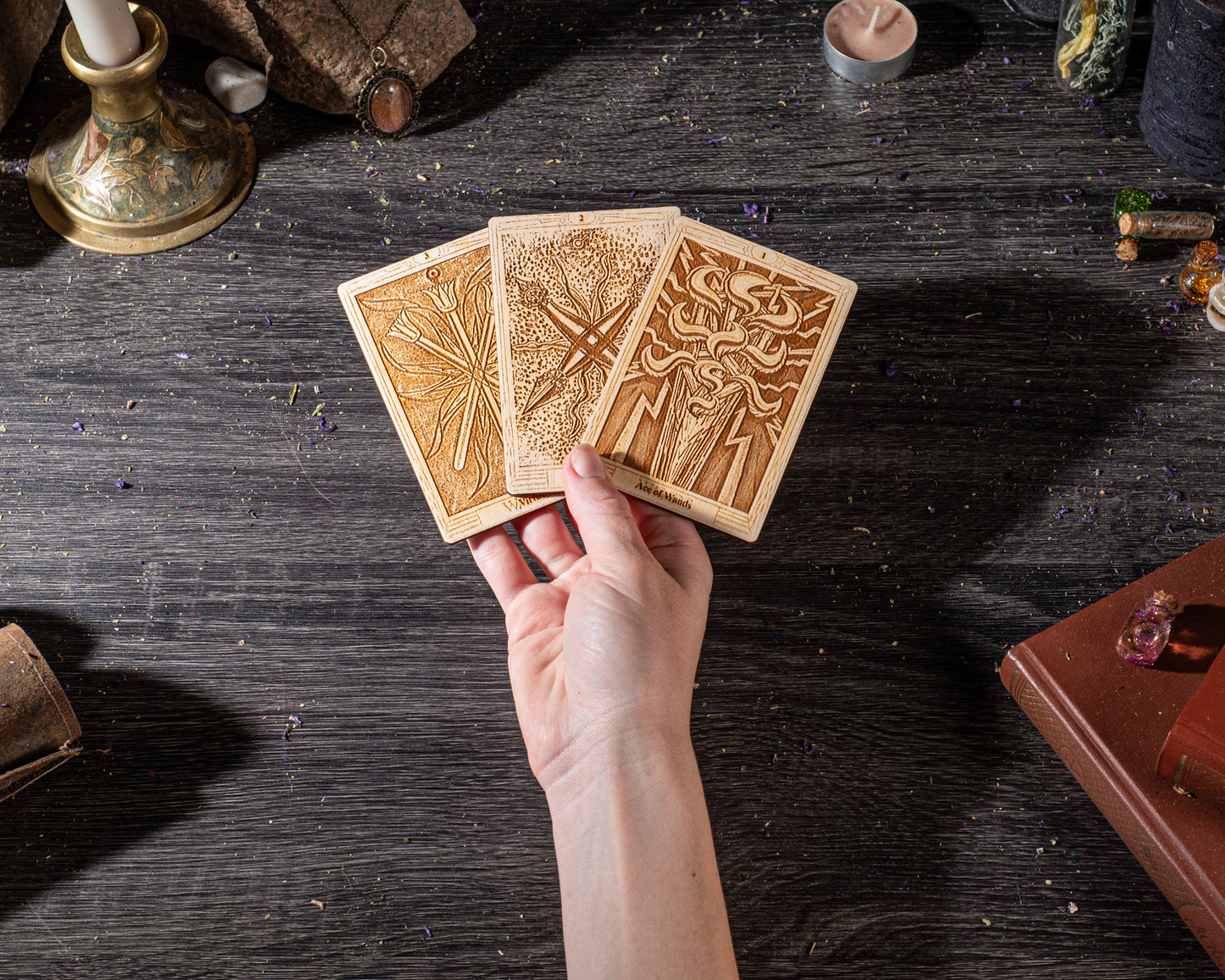 A hand is holding three wooden tarot cards against a dark wooden background.